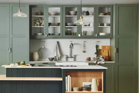 Stylish glass cabinet decor ideas in a modern kitchen with green cabinetry, showcasing ceramic bowls, plates, and glassware.